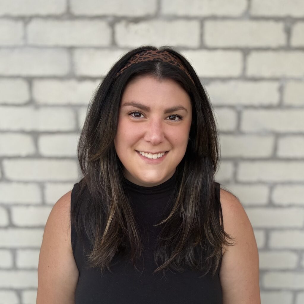 Professional headshot of Deena, founder and lead coach at DFN Connected Growth Coaching, smiling warmly against a white brick wall.