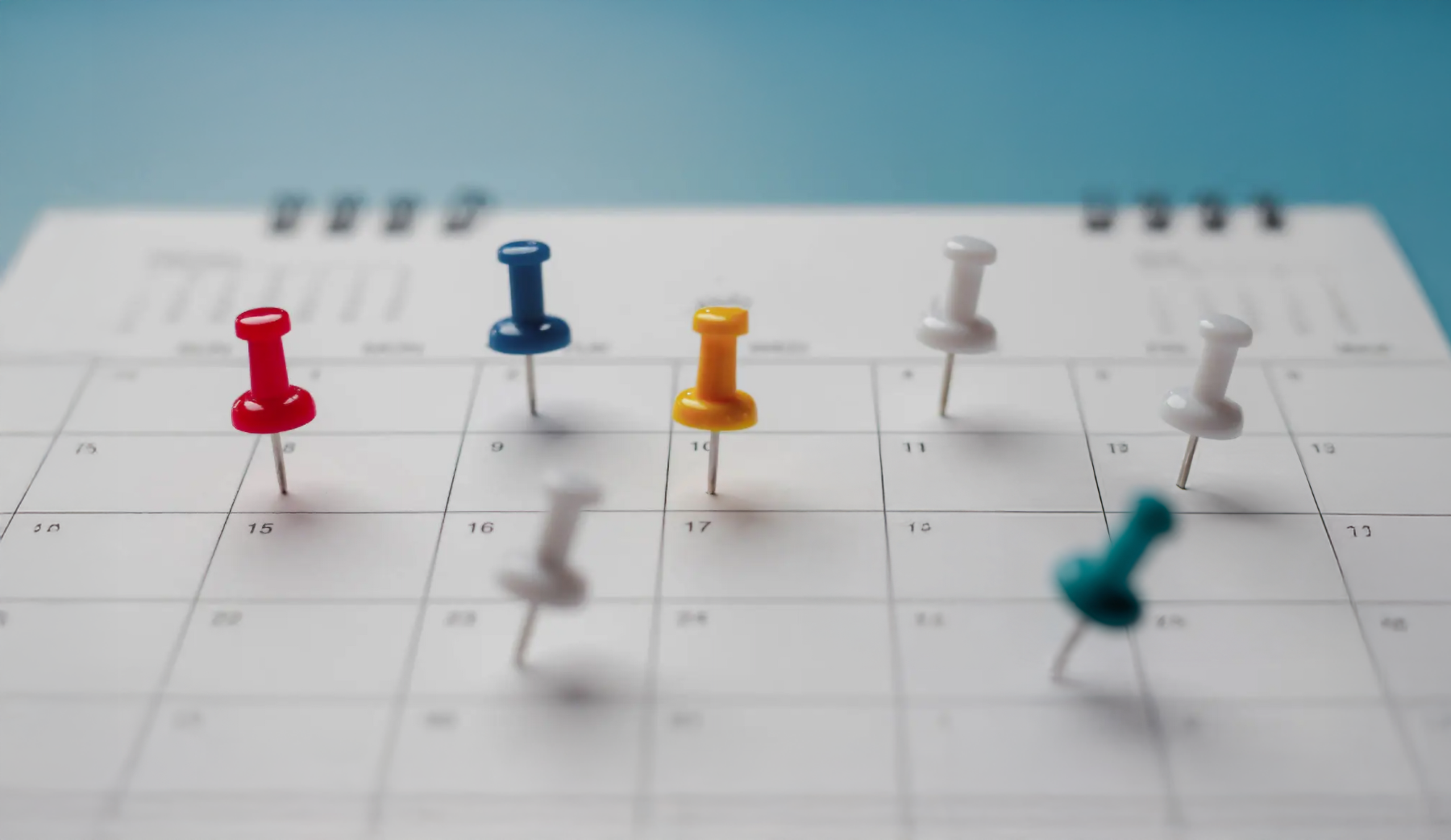 Colorful pushpins marking dates on a white desk calendar against a blue background.